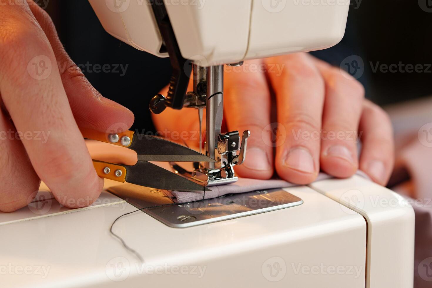 Hands sewing fabric using a sewing machine on a wooden table in a well-lit workspace photo