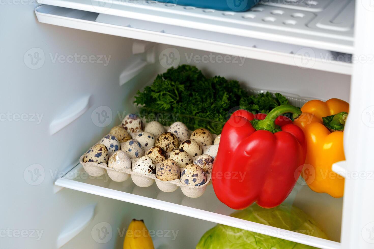 Open Refrigerator With Fresh Produce, Eggs, And A Blue Container photo