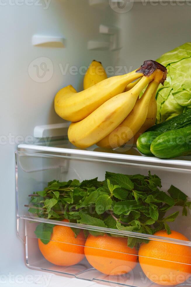 Open Refrigerator With Fresh Produce, Eggs, And A Blue Container photo