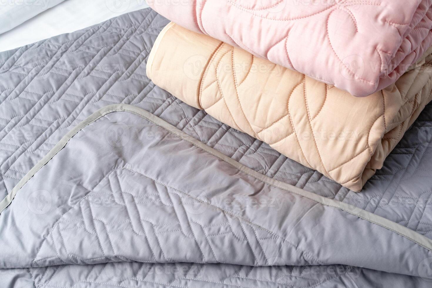 Stacked Pink And Peach Quilted Blankets On A Gray Bed photo
