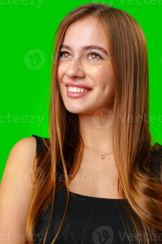 Smiling Young Woman With Long Brown Hair Looking Up Against Green Screen photo