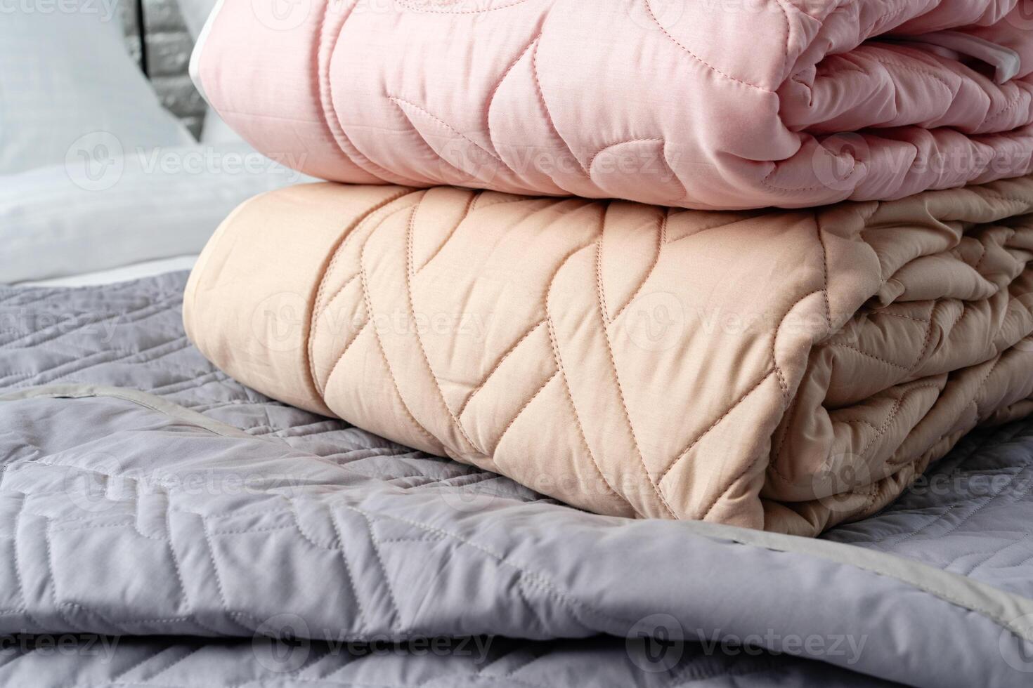Stacked Pink And Peach Quilted Blankets On A Gray Bed photo