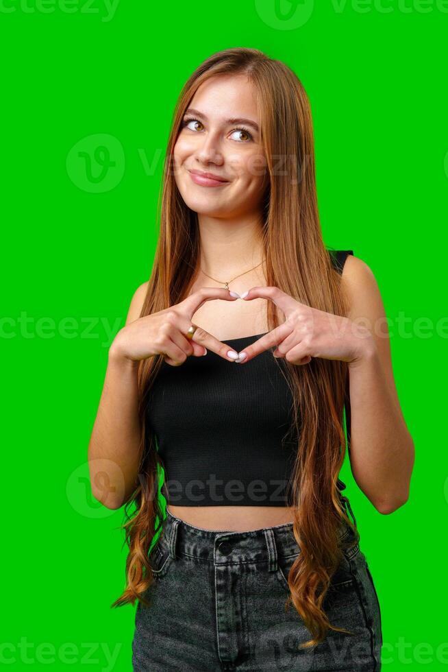 Young Woman Making Heart Shape With Hands Against Green Screen photo