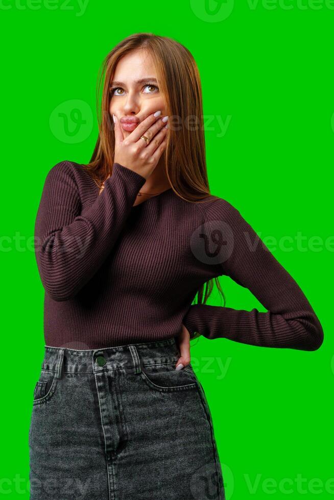 Young Woman With Brown Hair Wearing a Maroon Sweater and Denim Skirt Posing Against a Green Screen photo