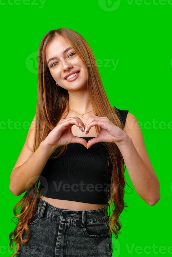 Young Woman Making Heart Shape With Hands Against Green Screen photo