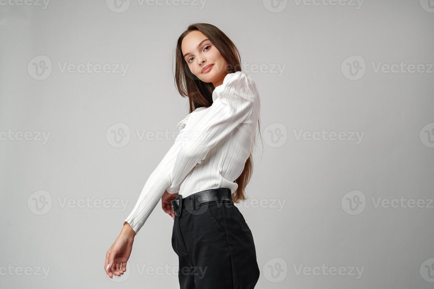 Young Woman in White Blouse and Black Pants Posing Against a White Background photo