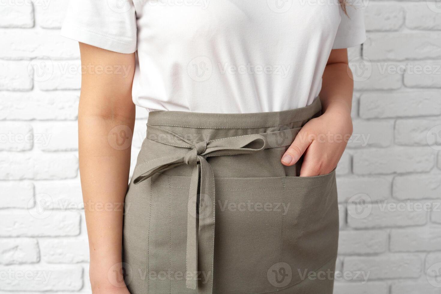 Woman Wearing a Gray Apron With a White T-Shirt in Front of a White Brick Wall photo