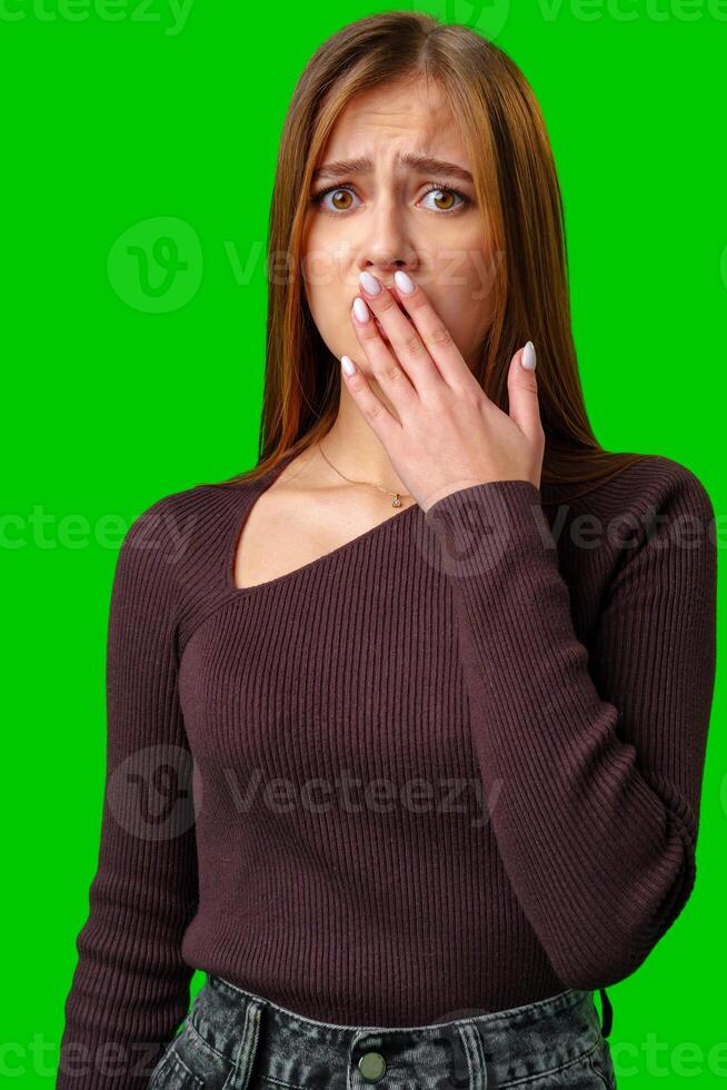 Young Woman Covering Mouth In Surprise Against Green Screen photo