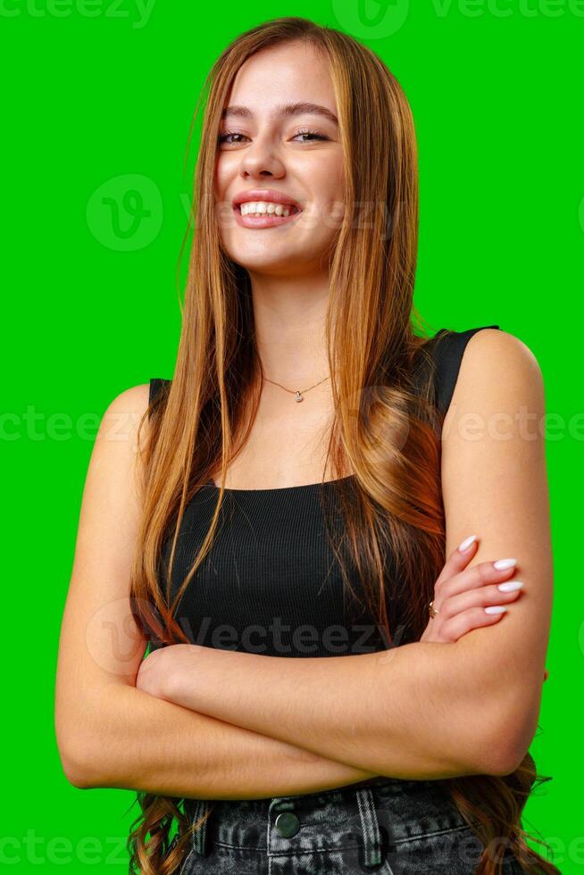 Young Woman With Long Brown Hair Smiles With Arms Crossed Against Green Screen photo