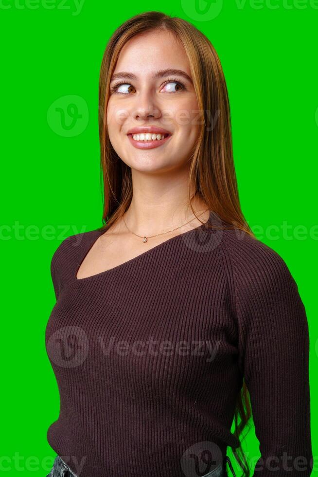 Young Woman Wearing Brown Sweater Looking Up and Smiling in Front of Green Screen photo