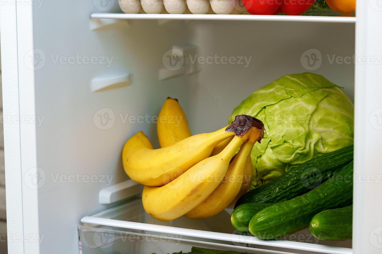 Open Refrigerator With Fresh Produce, Eggs, And A Blue Container photo