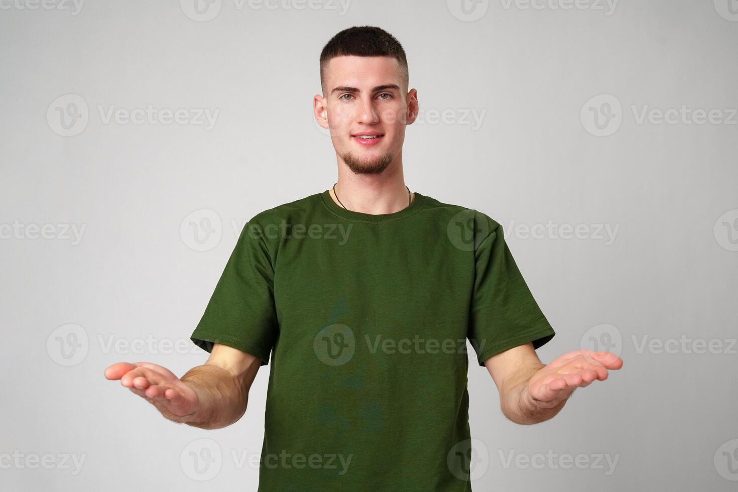 Young Man Wearing Green T-Shirt Gesturing With Both Hands in Front of a Plain White Background photo