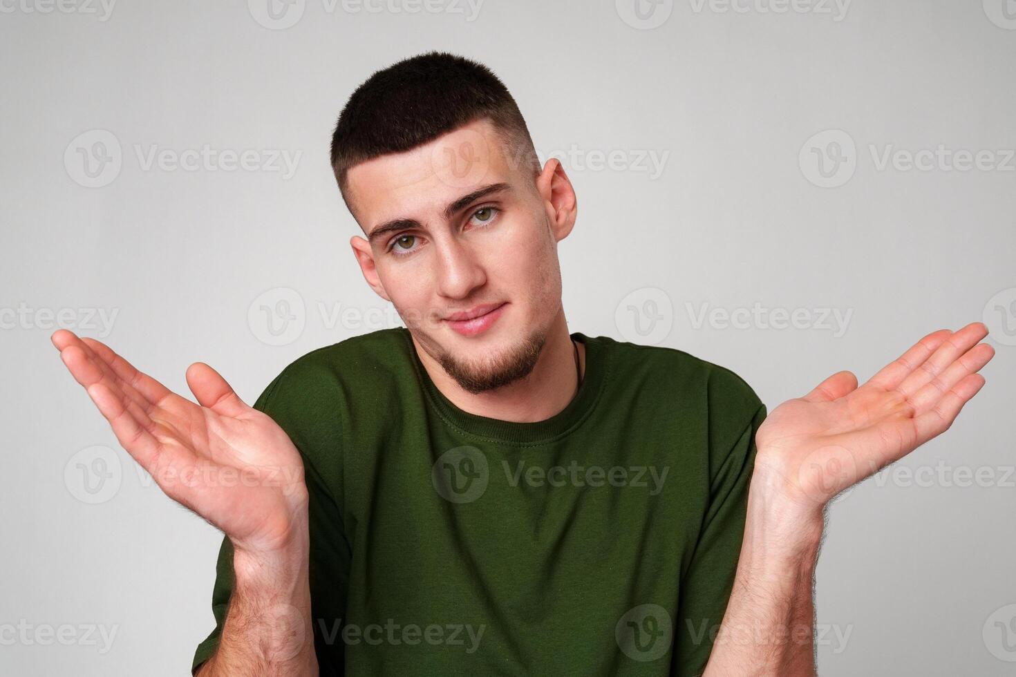 Young Man Wearing Green T-Shirt Gesturing With Both Hands in Front of a Plain White Background photo