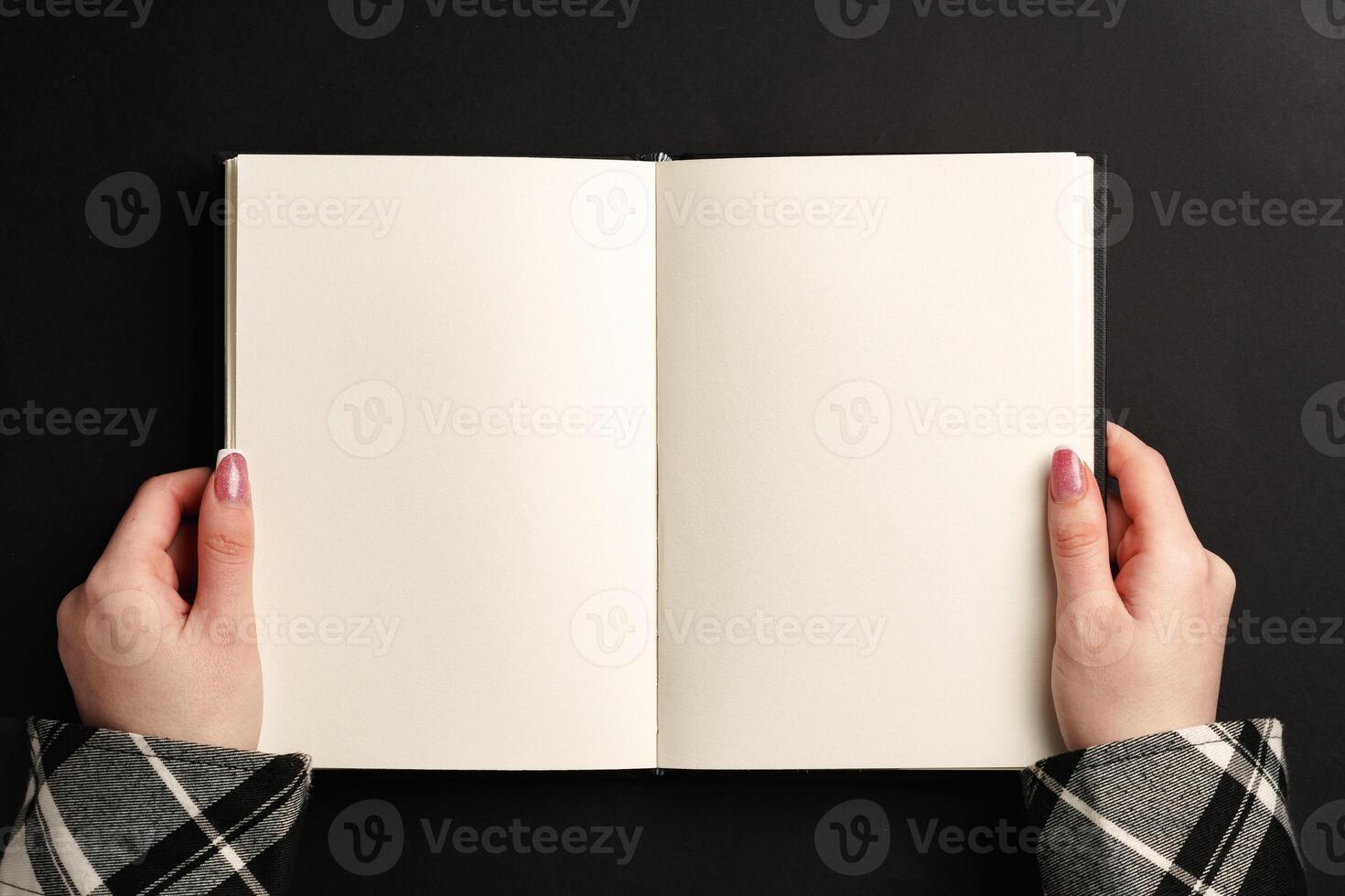 Open notepad in hands on black background photo
