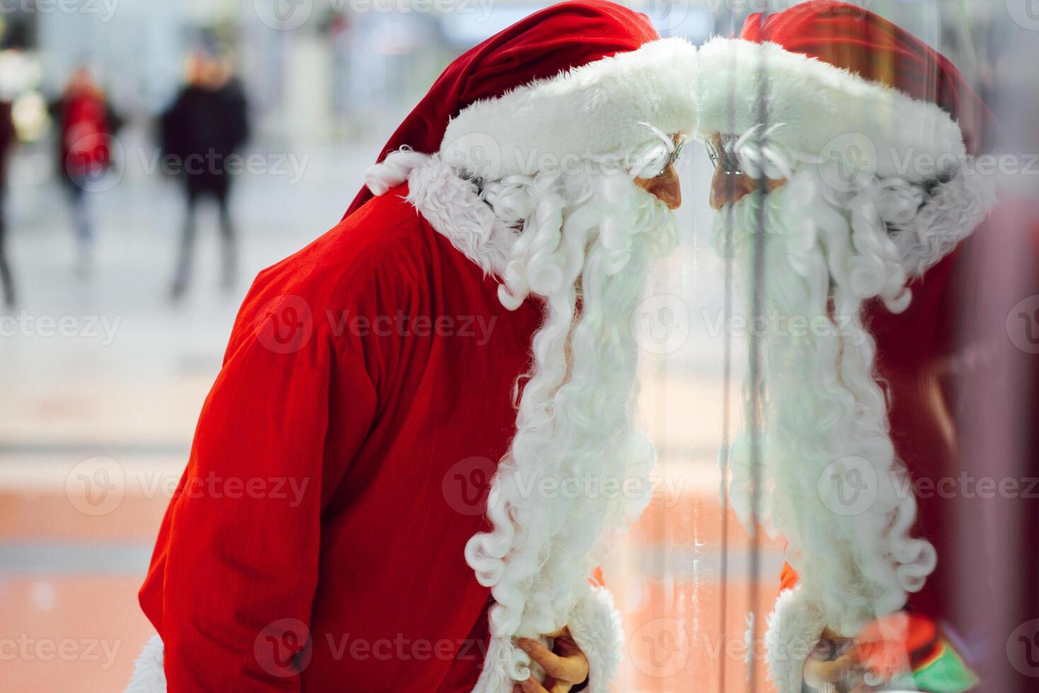 christmas, holidays, gesture and people concept - man in costume of santa claus waving hand over shopping center background photo
