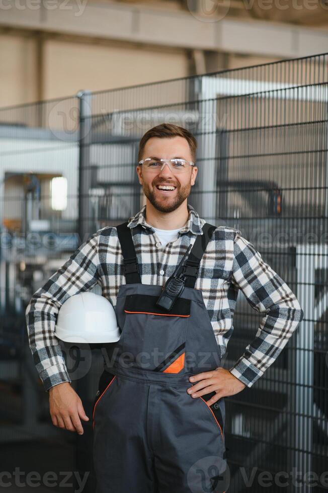 Smiling and happy employee. Portrait of industrial worker indoors in factory. Young technician with white hard hat photo