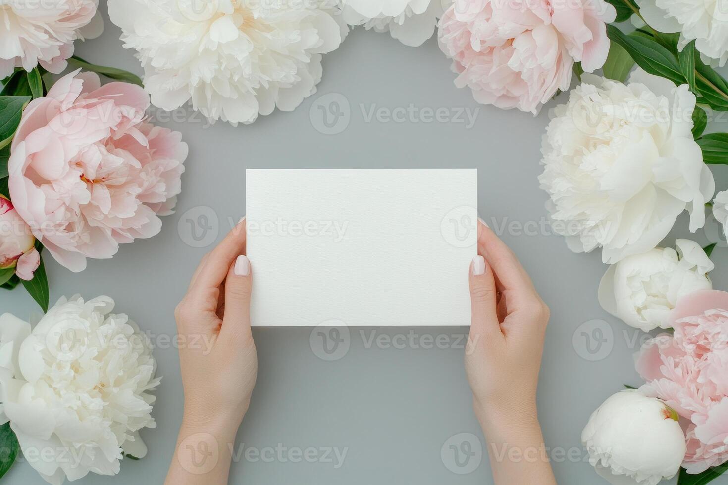 Elegant wedding invitation with pink and white peonies on a soft grey backdrop featuring hands holding a blank card photo