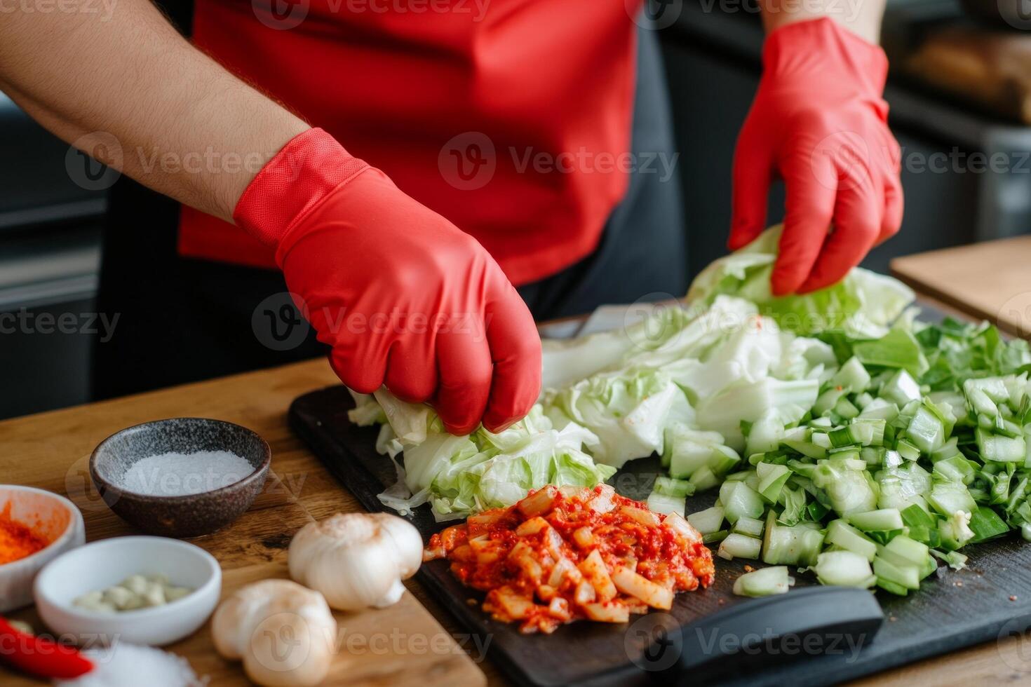 Hands in red gloves mixing spicy chili paste with Napa cabbage for traditional kimchi on wooden table photo