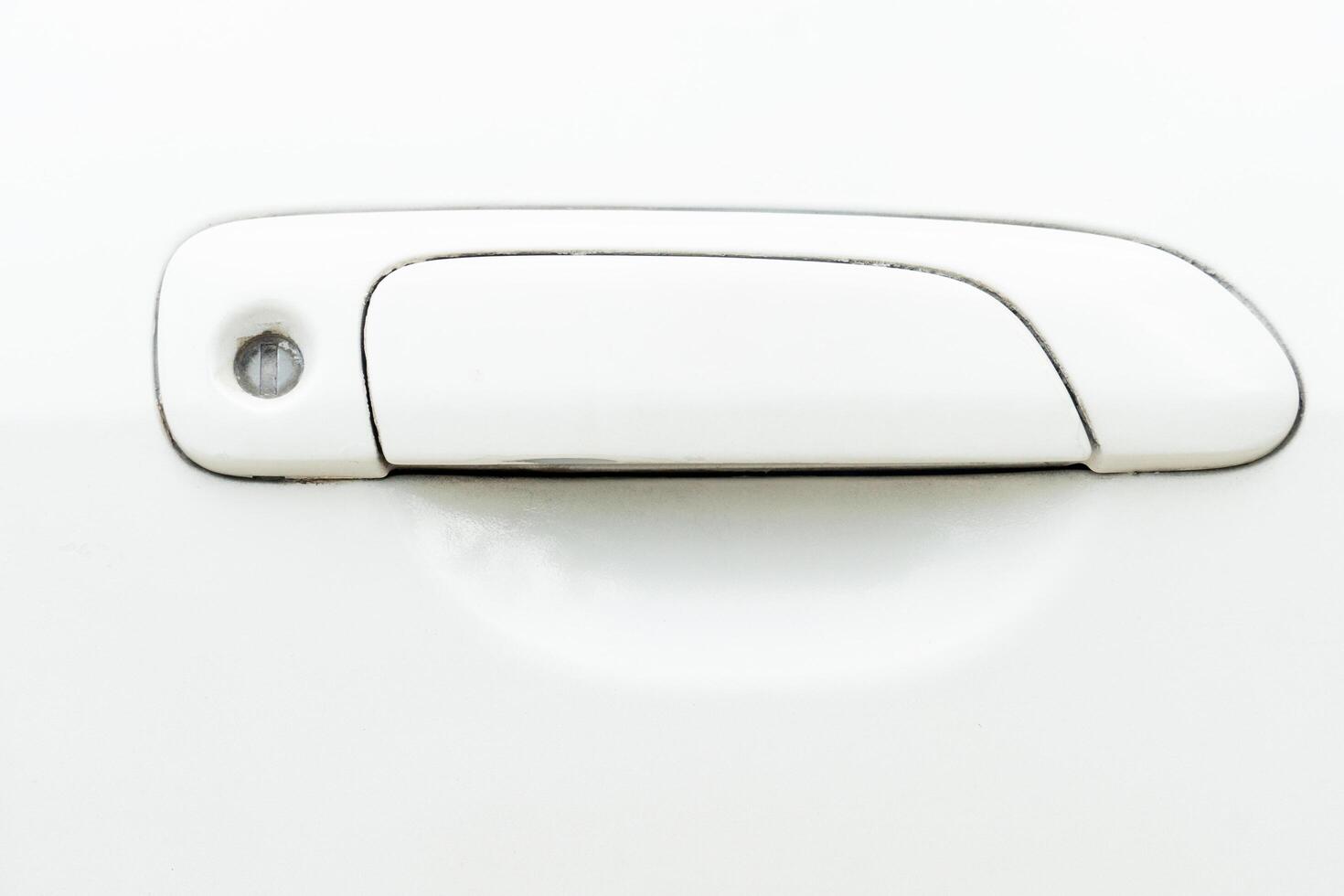 View of a used white car door handle. handle itself is a rectangular shape with a slight curve at the bottom. Round hole at the top end of the handle likely for a keyhole. Stains in the keyhole. photo