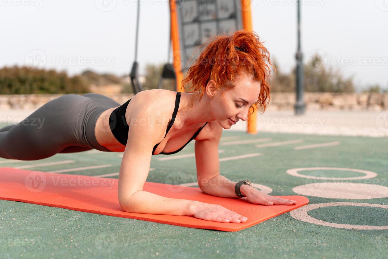 Determined woman practicing plank position on mat at outdoor gym photo