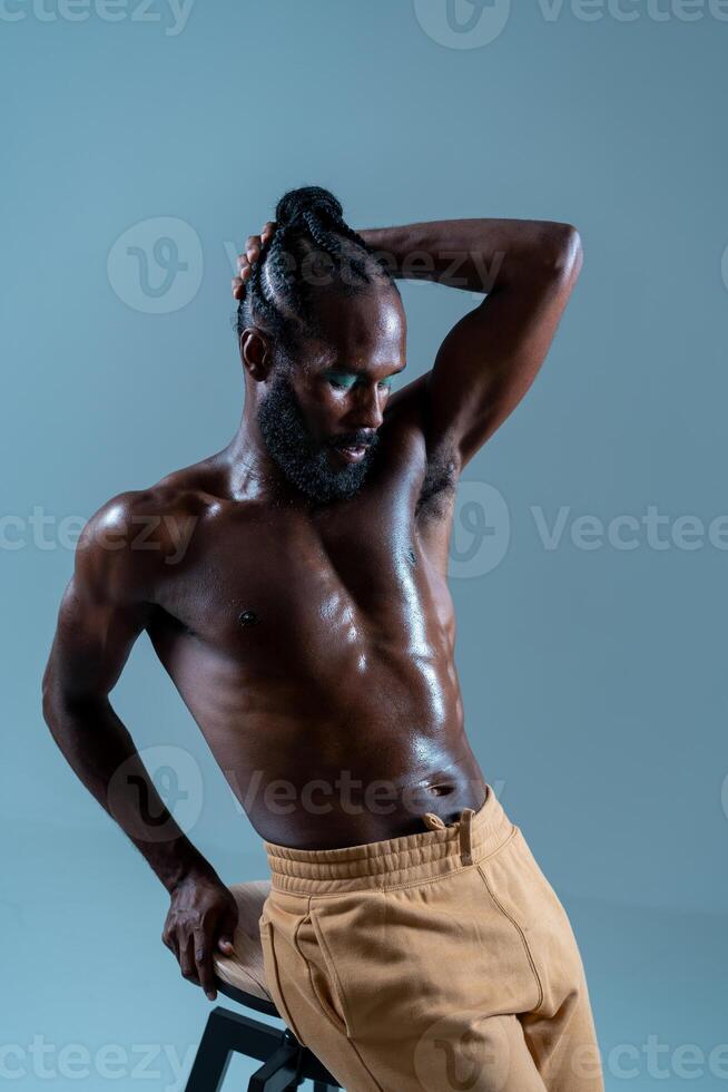 Black shirtless gay model posing while leaning on stool in studio photo