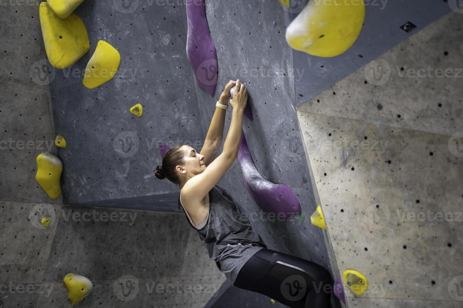 Determined woman climbing artificial rock wall at bouldering gym photo