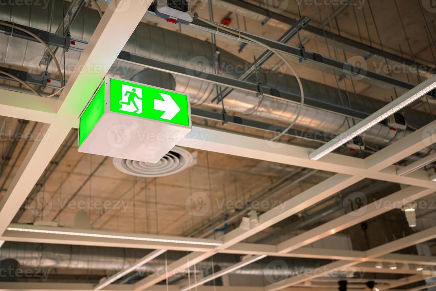 Selective fire exit sign on ceiling. Green fire escape sign hang on the ceiling. Green emergency exit sign showing the way to escape.Fire exit in the building. photo