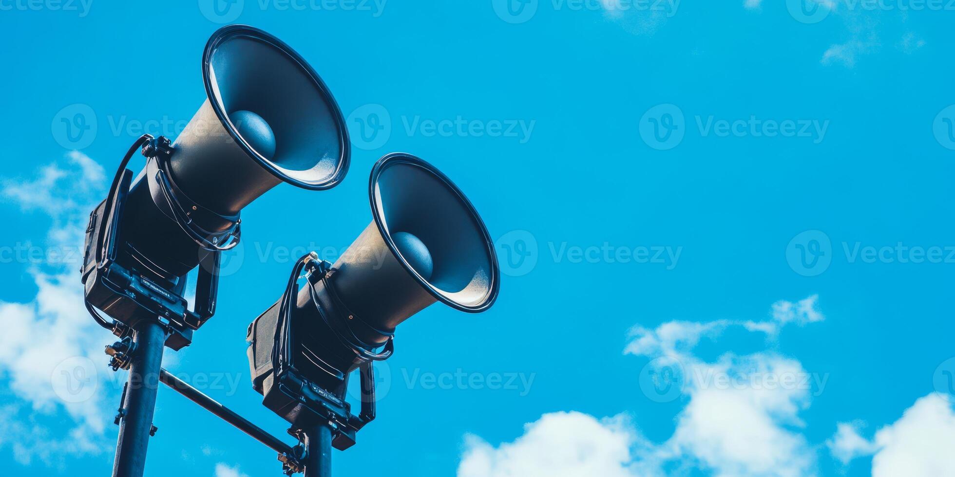 Two loudspeakers are mounted on a pole against a blue sky, designed for public announcements and alerts in urban areas, ensuring effective community communication in various situations photo