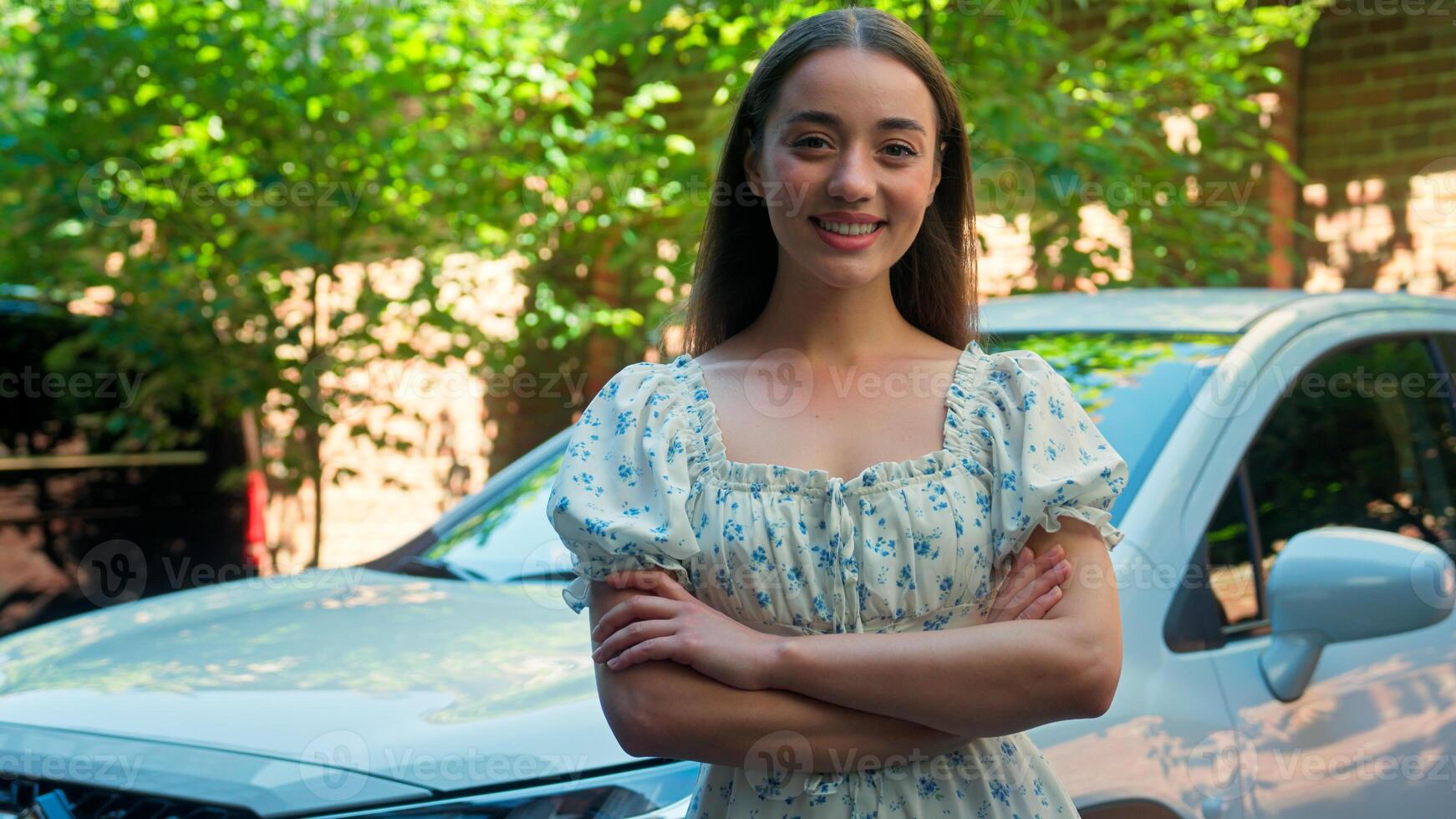 Confident successful happy Caucasian smiling woman girl female owner client looking at camera crossing hands crossed arms posing with new car buying automobile rental service test drive at city street photo
