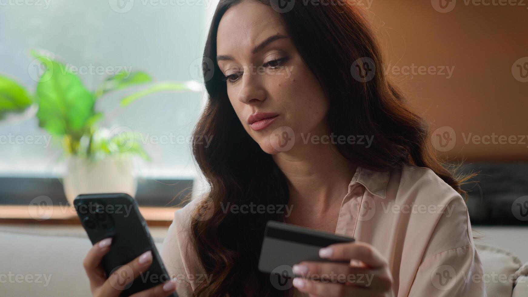 Caucasian girl upset irritated woman angry female on sofa hold credit card use mobile bank app phone try to pay online banking problems no money insecure payment scam fraud unsuccessful transaction photo
