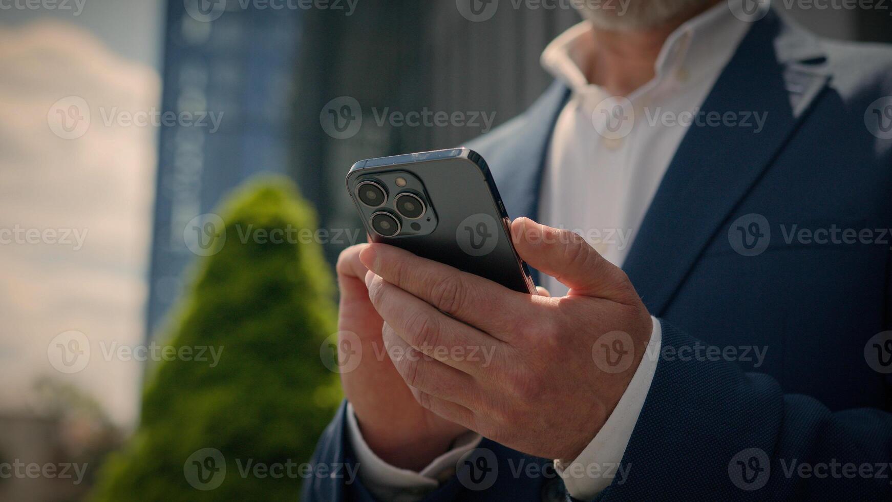Happy smiling mature employer middle-aged senior Caucasian entrepreneur outdoors old business man looking to side smile typing scrolling at mobile phone male businessman in city browsing smartphone photo