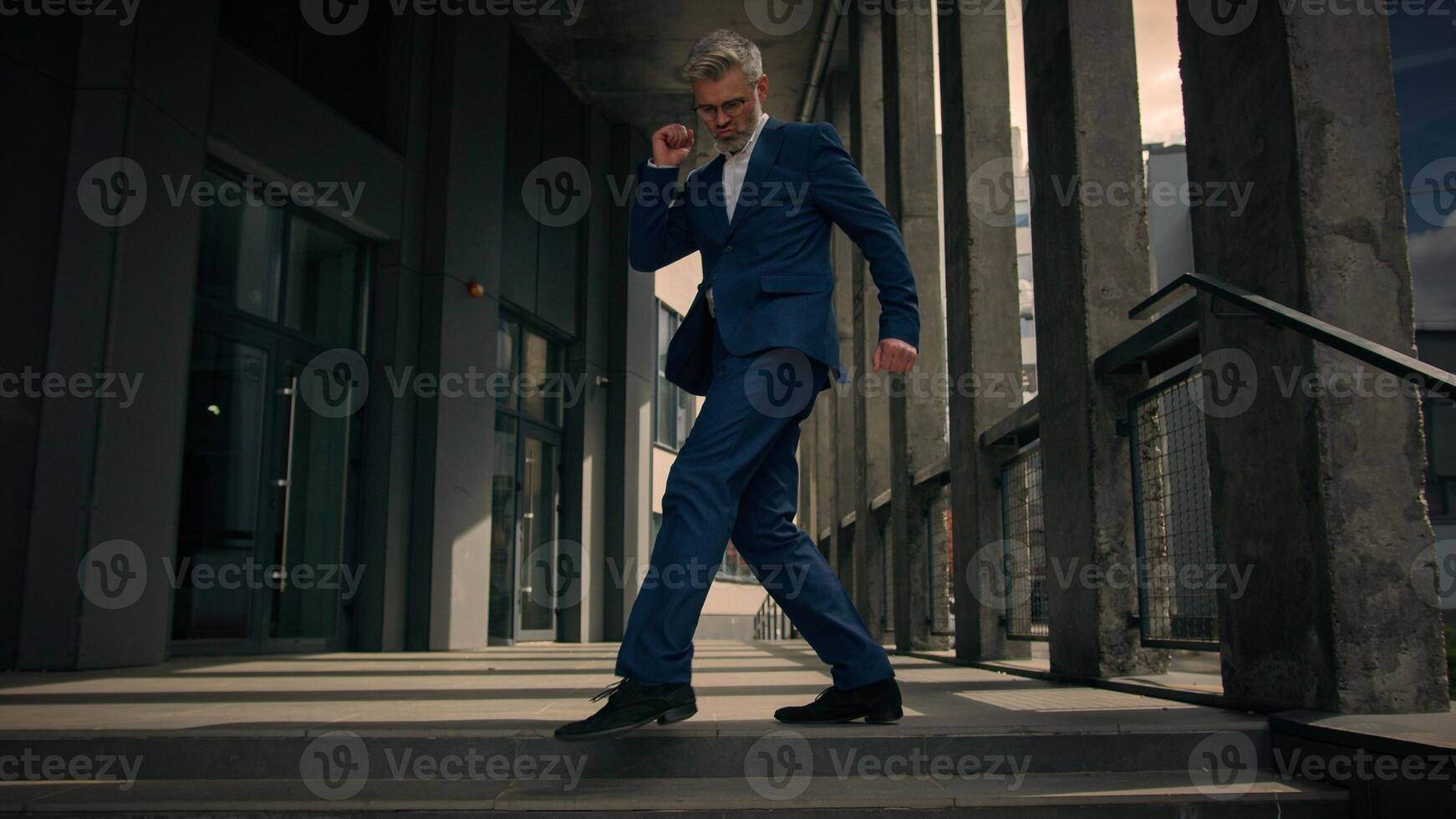 Funny moving happy Caucasian senior business worker employee mature man businessman dancing walking on stairs near office building outdoors walk dance celebrate achievement having fun fooling around photo