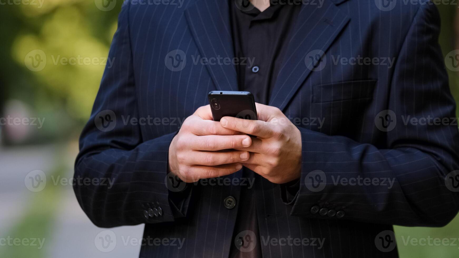 Close up male hands unknown man in black formal suit hold smartphone chatting in social media use mobile app chat texting message search information in internet scroll website page play internet game photo
