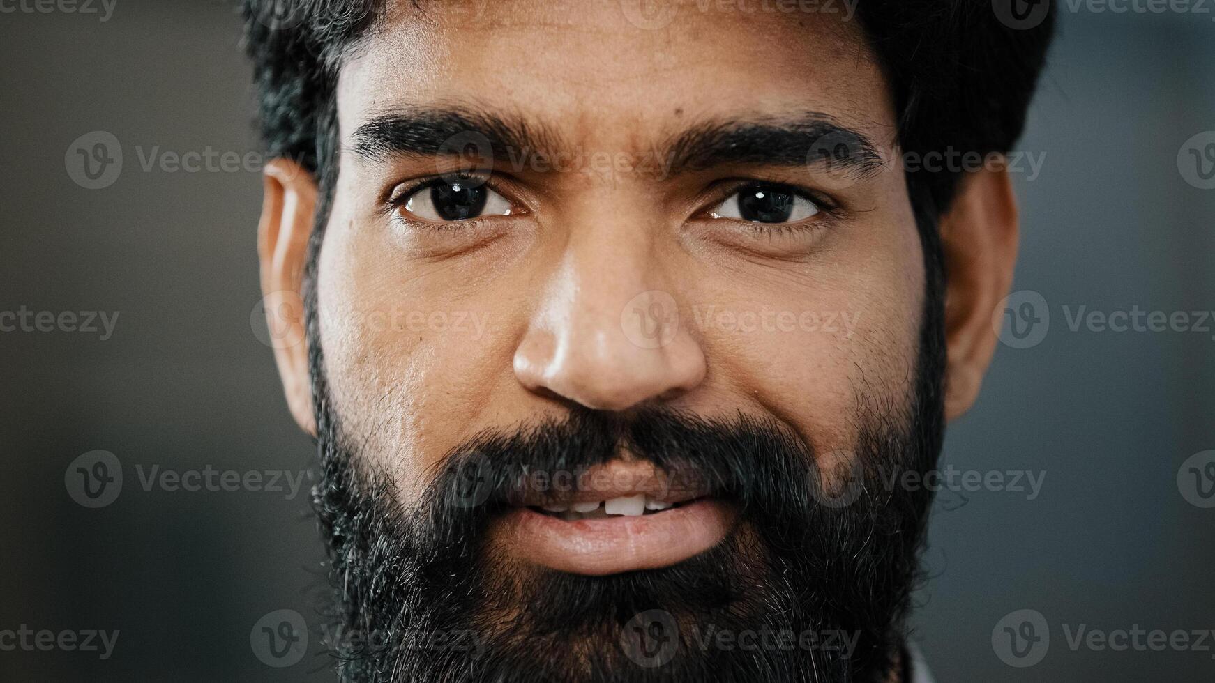 Close up portrait male bearded face adult brunet man with dark brown eyeballs looking at camera smiling hispanic indian positive young guy handsome intelligent person having good mood posing indoors photo