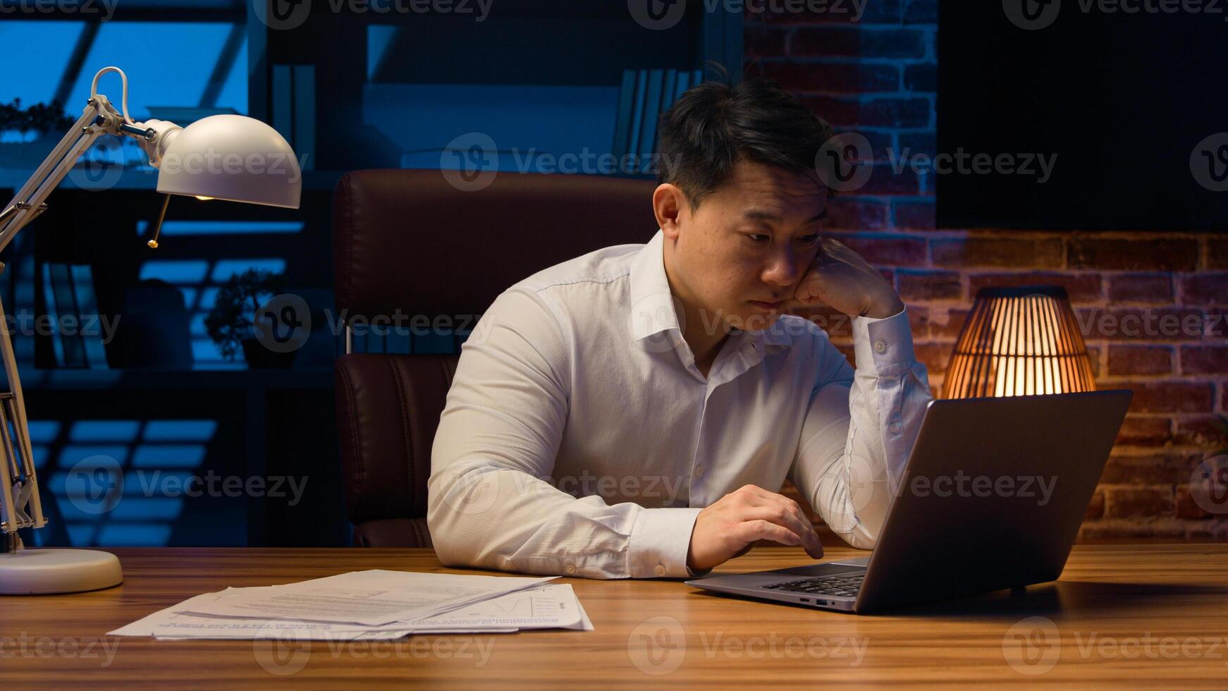 Exhausted fatigued tired Asian man manager office worker at night evening overworked deadline job project working with boring laptop startup sleepy businessman Korean employer drowsy boredom stressed photo
