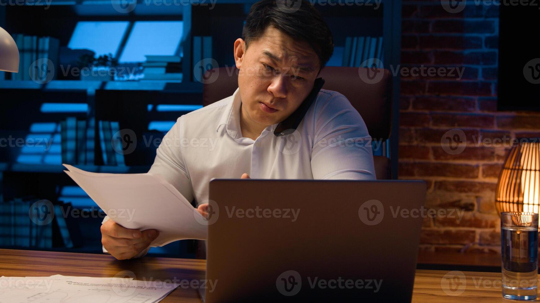 Angry disappointed Asian businessman mad aggressive talking mobile phone at night evening office dissatisfied with business documents papers mistake stressed Korean man executive manager arguing call photo
