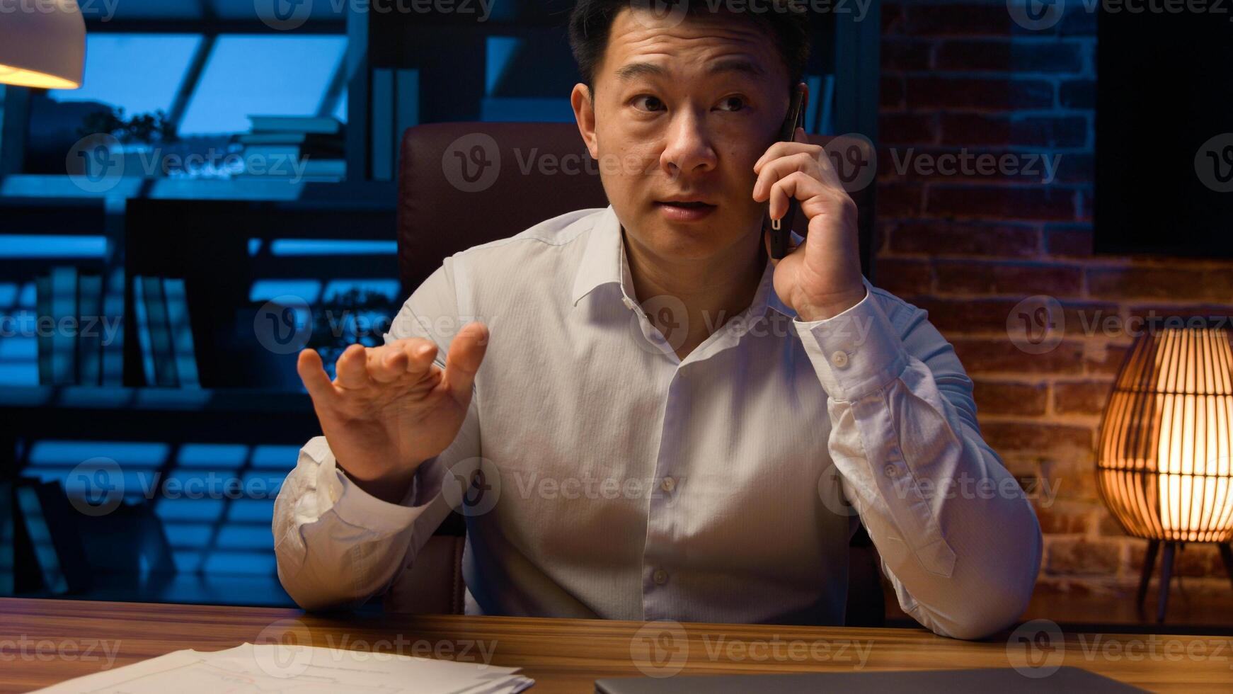 Angry disappointed business employer Asian businessman mad dissatisfied Chinese man stressed Korean entrepreneur argue conflict quarrel misunderstanding talking mobile phone at night evening office photo