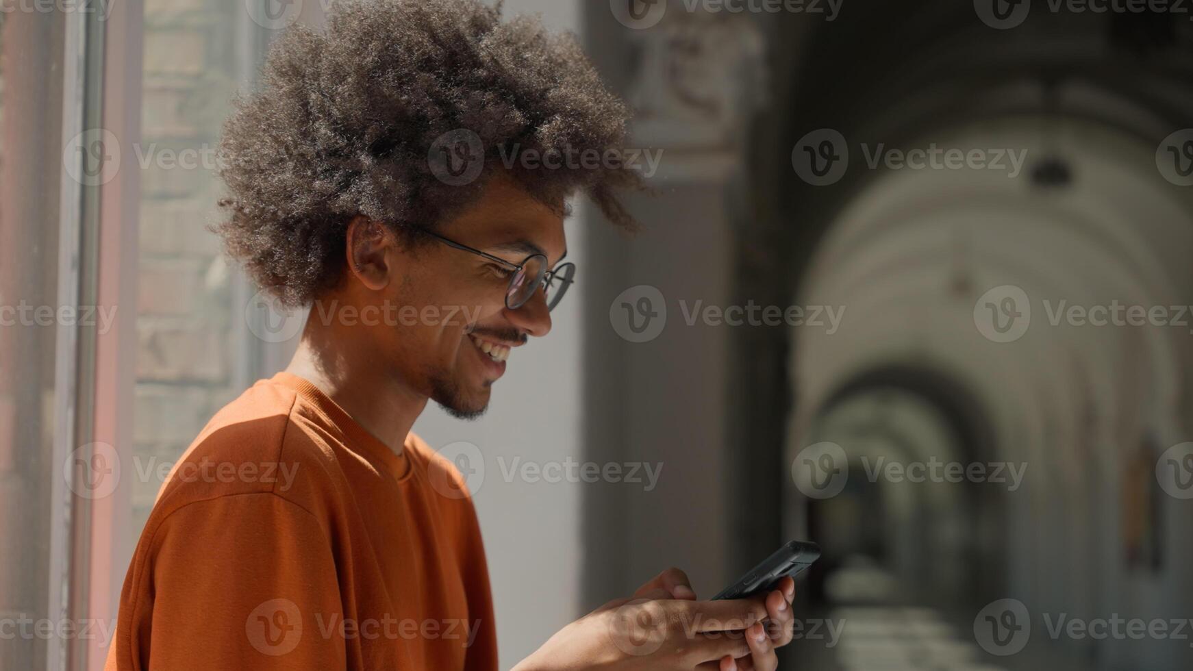African American ethnic guy male man student using mobile phone in college university high school scrolling smartphone smiling happy e-commerce social media addict study education break gadget online photo
