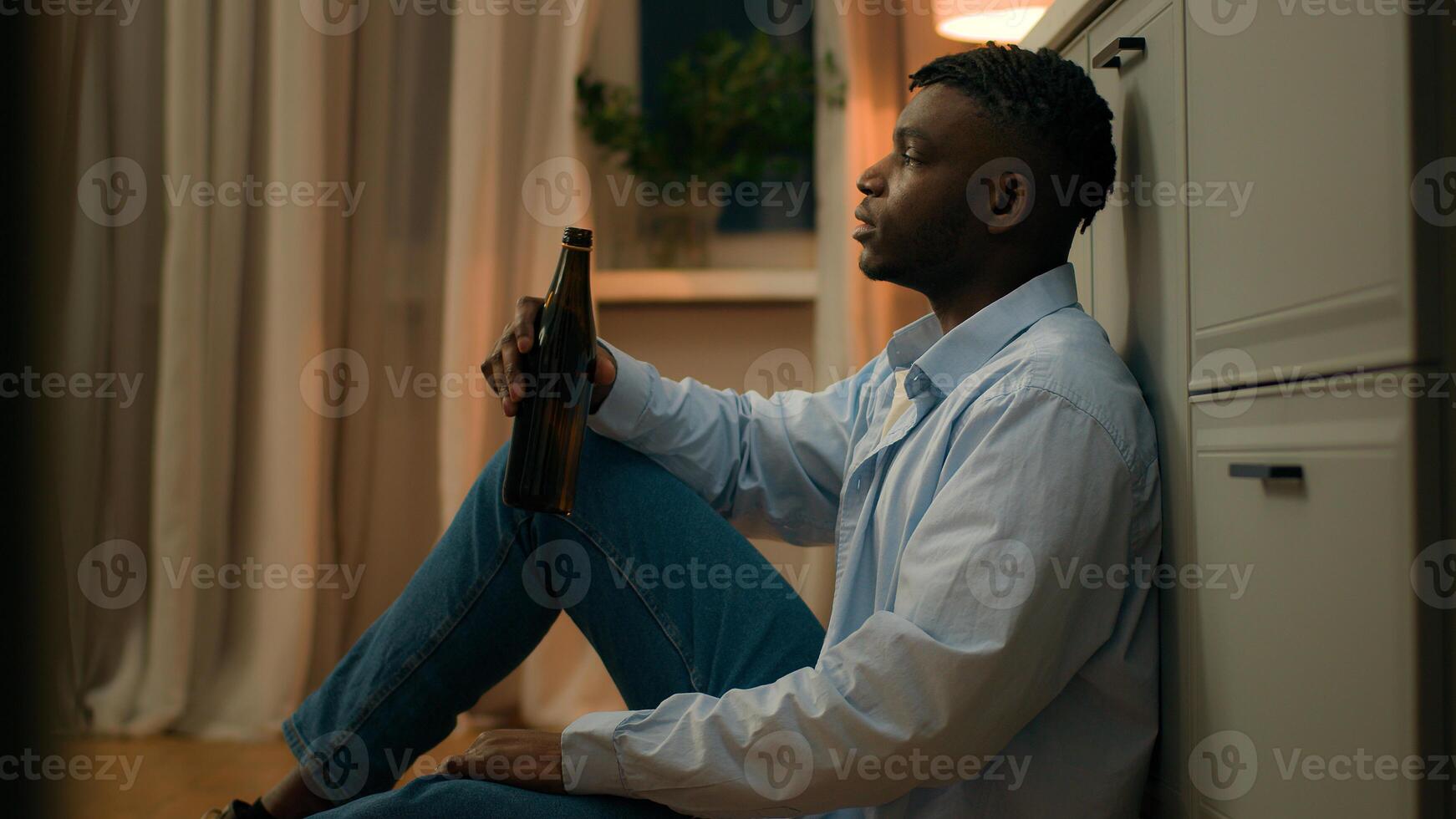 Sad upset African American man drunk male addicted guy alcohol addiction drinking beer alone at home kitchen evening on floor suffer heartbreak divorce health problem alcoholism bankruptcy loan lost photo