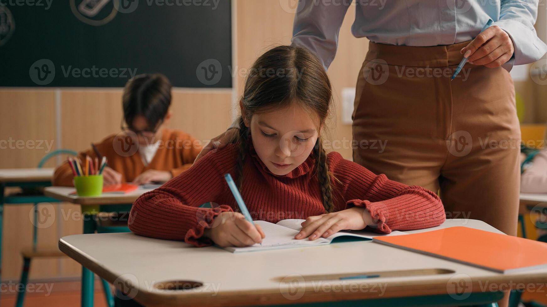 School class lesson children studying learning in classroom woman teacher female tutor walking teaching little boy child kid rise hand ask help question answer study learn write talking education photo