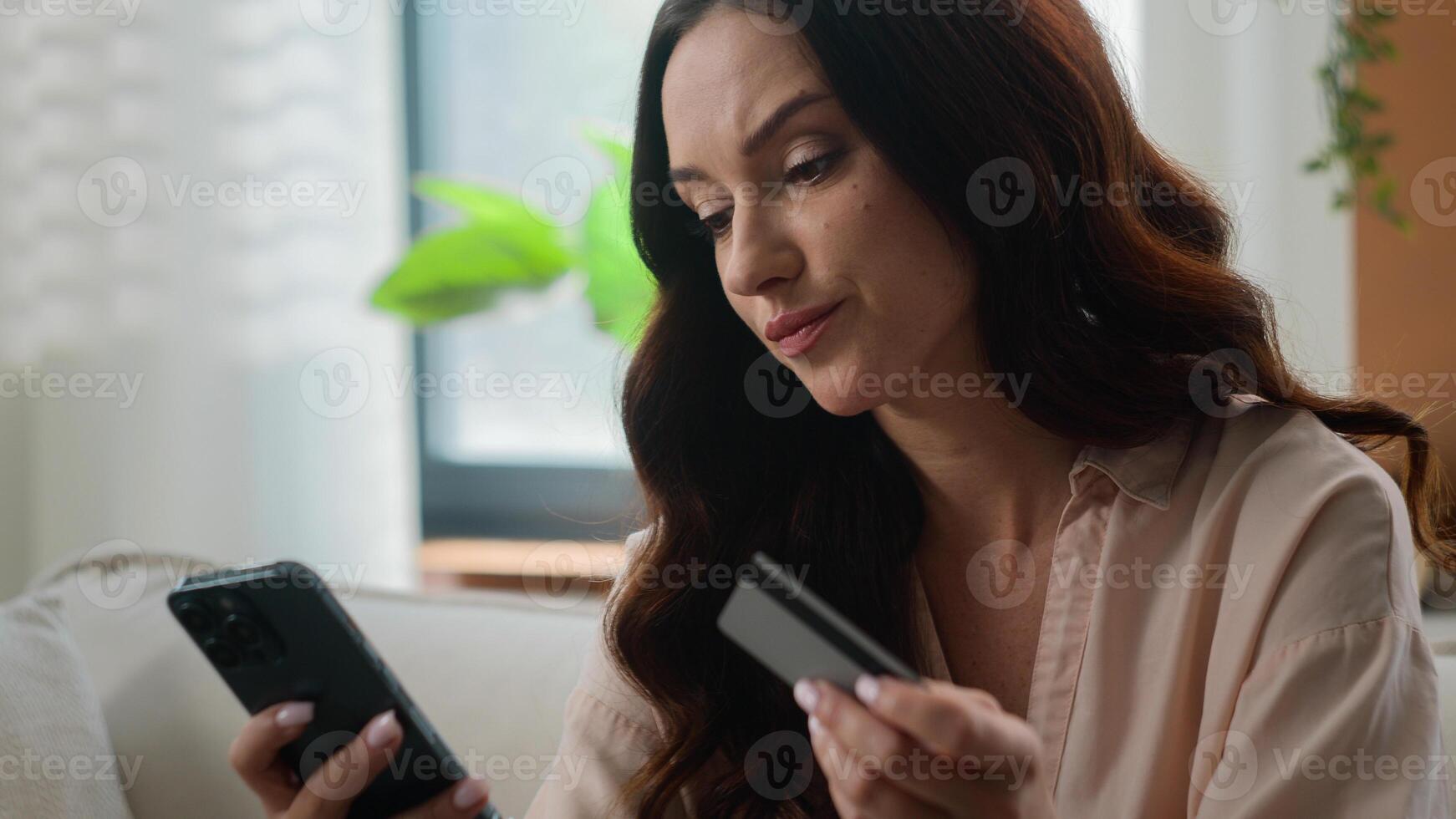 Caucasian girl upset irritated woman angry female on sofa hold credit card use mobile bank app phone try to pay online banking problems no money insecure payment scam fraud unsuccessful transaction photo