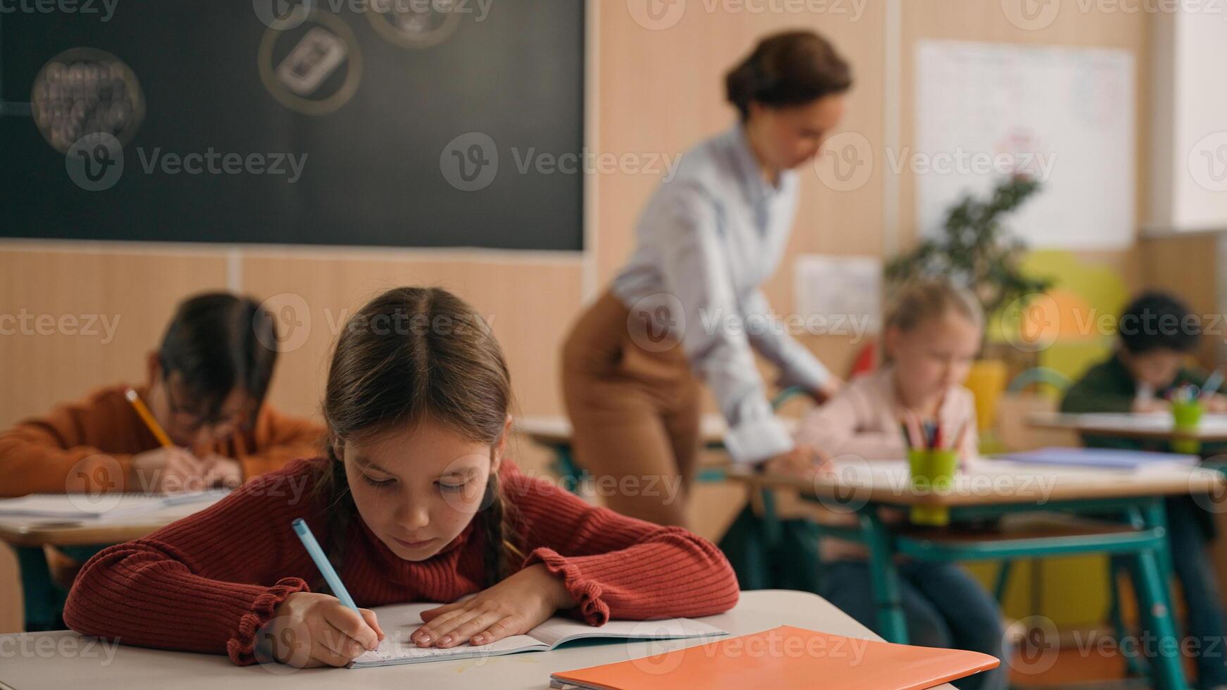 School class lesson children studying learning in classroom woman teacher female tutor walking teaching little boy child kid rise hand ask help question answer study learn write talking education photo