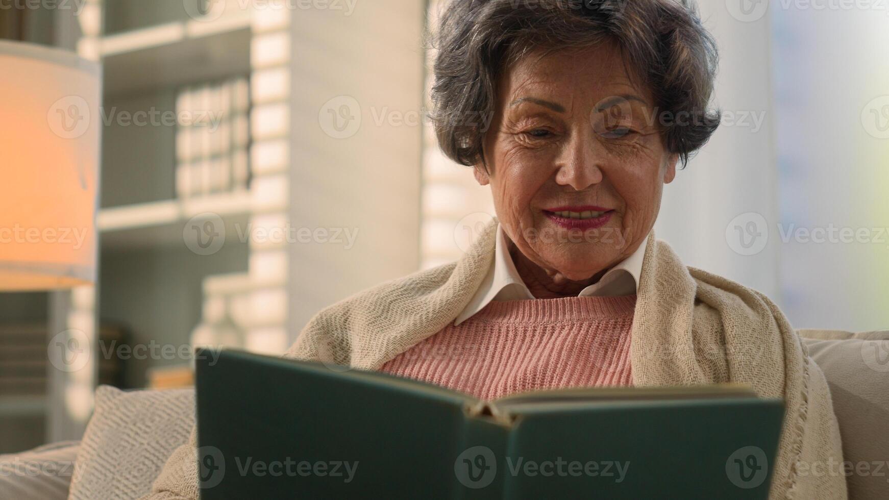 Happy inspired Caucasian old woman reading book smiling nostalgic senior mature lady elderly female retired pensioner grandmother read at home couch watching photos in album memory remember nostalgia