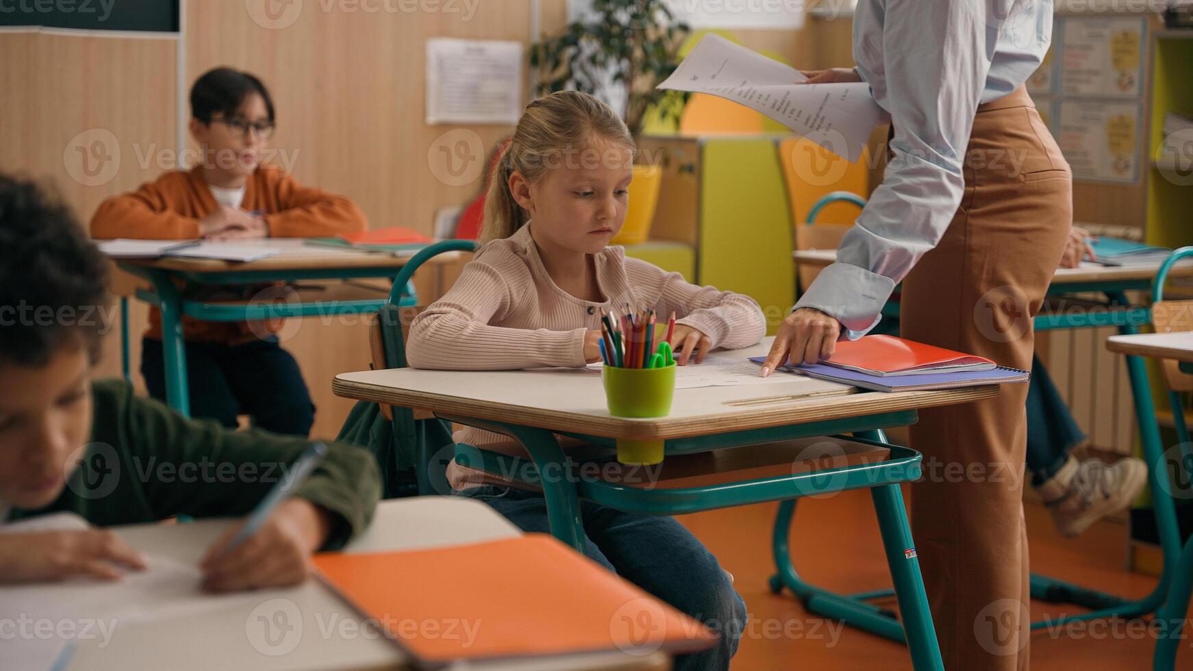School class lesson children studying learning in classroom woman teacher female tutor walking teaching little boy child kid rise hand ask help question answer study learn write talking education photo