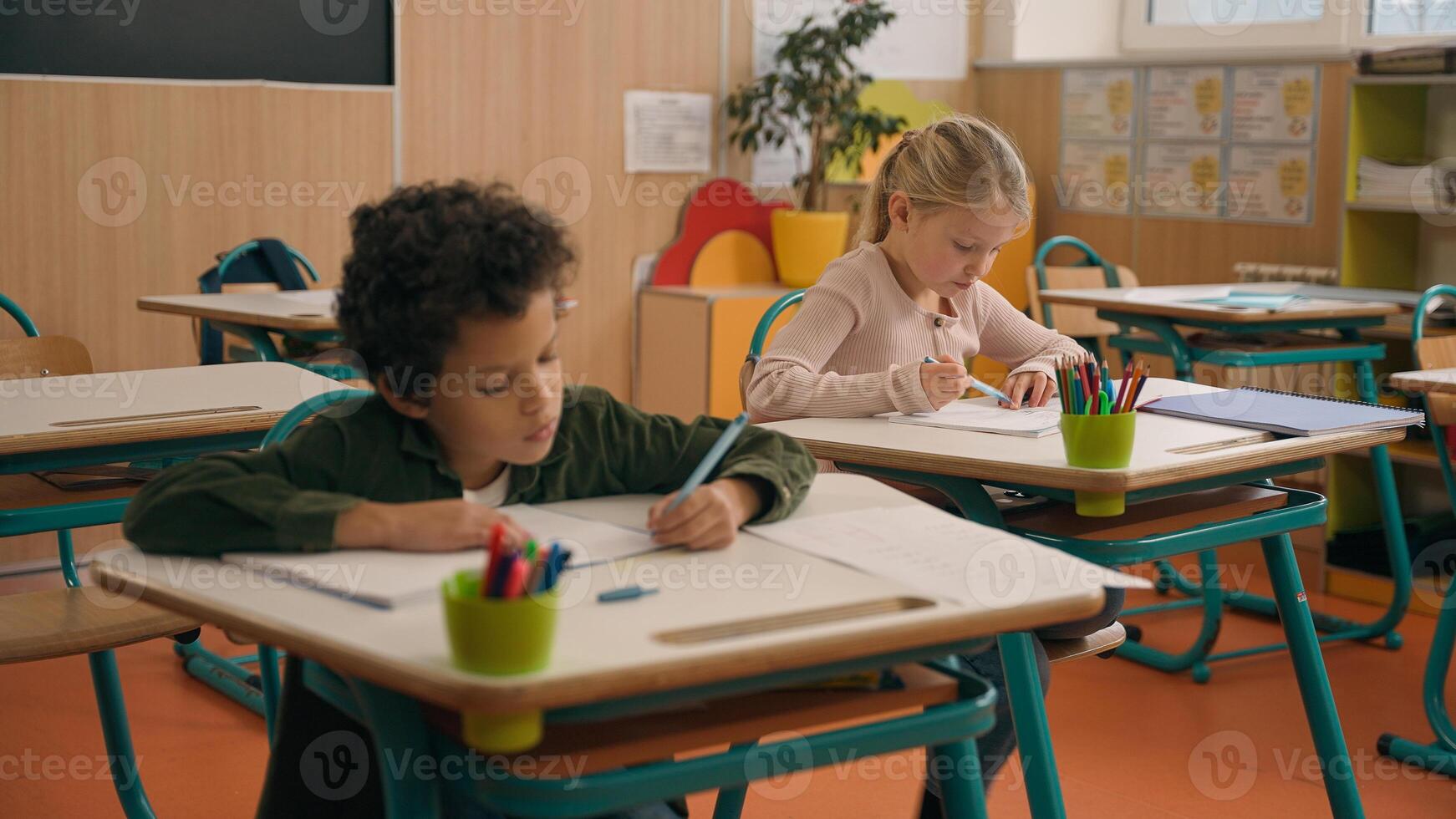 Elementary primary education studying in school multiracial pupils multiethnic children diversity kids African American son boy Caucasian girl daughter in classroom writing test exam write study learn photo