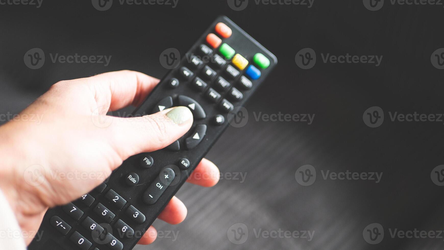A hand holding remote control fingers black buttons tv photo