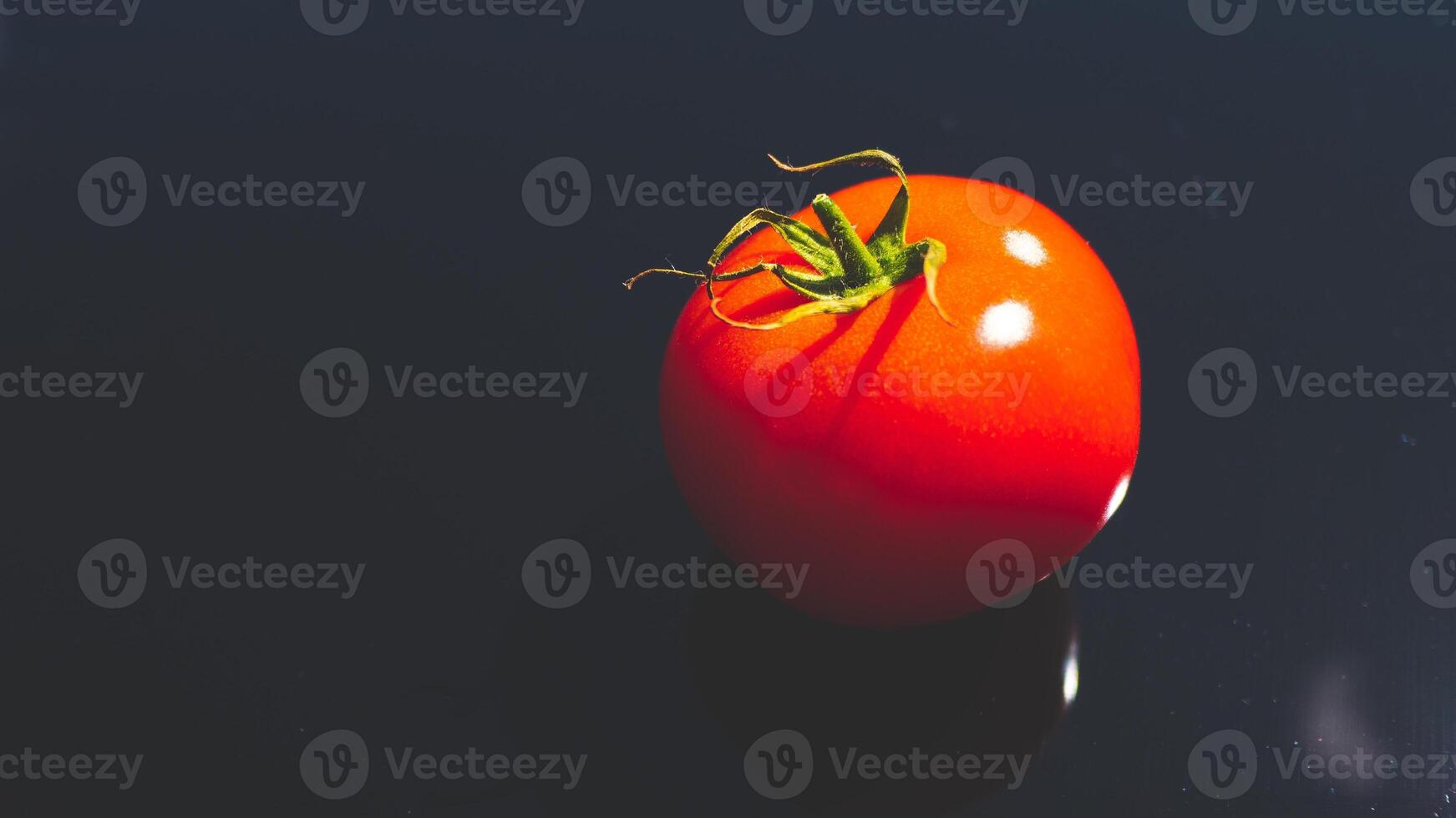 A tomato on black background glassy surface minimalist contrast vibrant colours photo