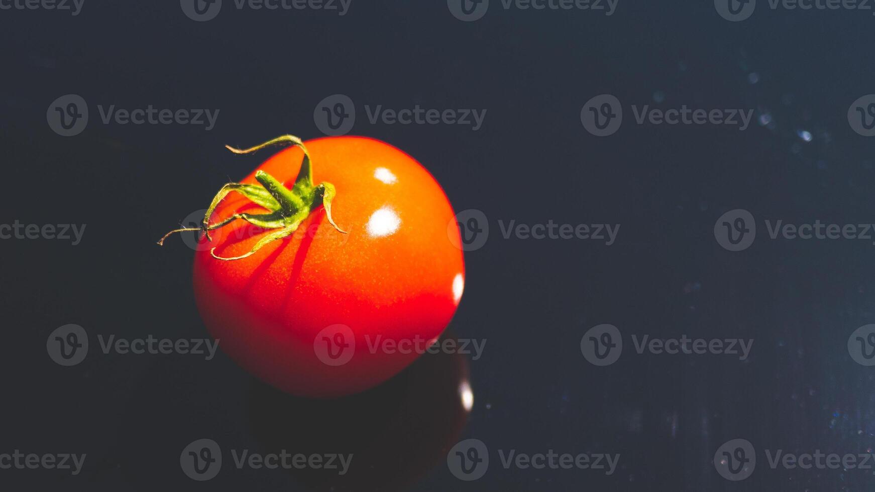 A tomato on black background glassy surface minimalist contrast vibrant colours photo
