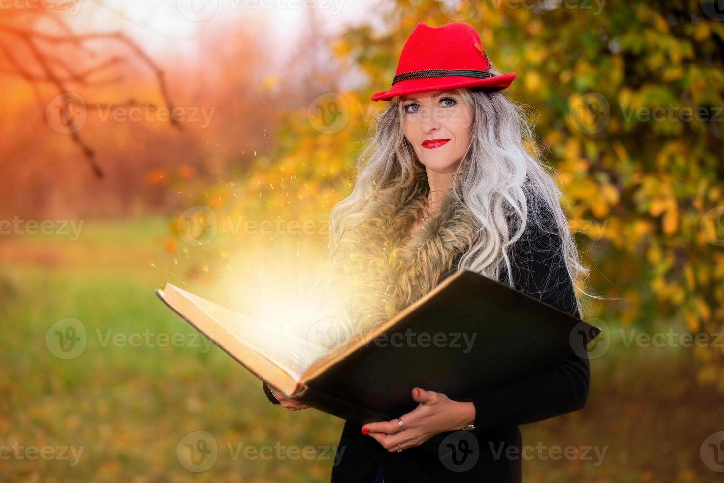 Halloween a woman with a book of magic spells in a witch's hat is conjuring, performing witchcraft against the background of an autumn forest. photo