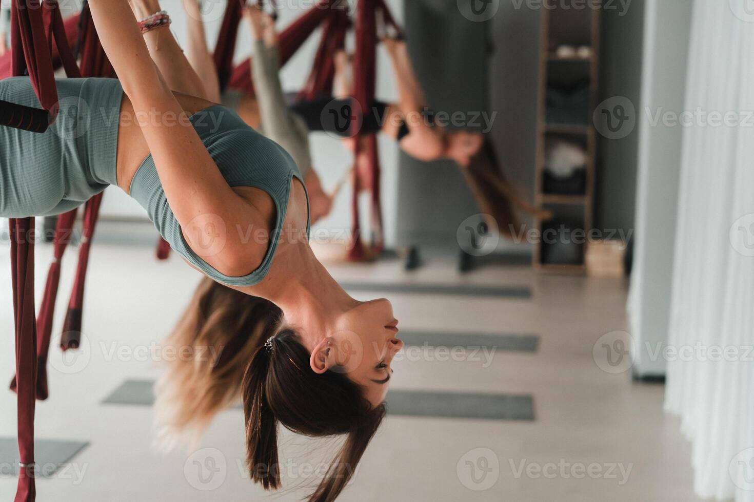 A group of women are hanging upside down on hanging hammocks. Fly yoga in the gym photo